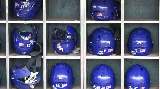 Blue baseball helmets with white numbers, including one for LSU’s Pearson, sit neatly in a cubby shelf highlighting summer stars.