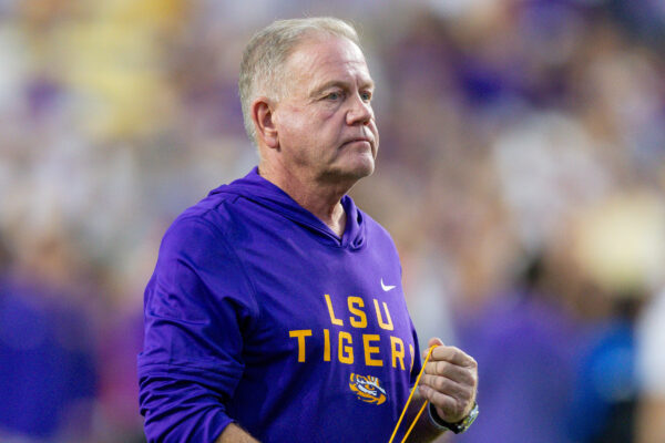 A man in a purple LSU Tigers hoodie stands outdoors with blurred stadium seats behind him, showing Louisiana sports pride.