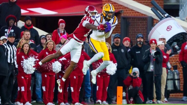 A Three Tigers player in yellow and white leaps to catch a pass as a red-uniformed defender tries to block him near the sideline.
