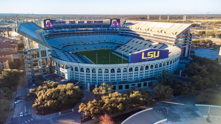 Aerial view of Louisiana's Tiger Stadium with empty stands, the field, scoreboards, and nearby trees and buildings visible.