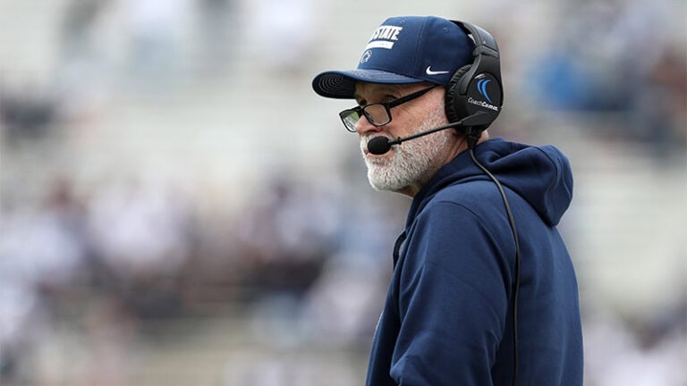 Jim Knowles stands on the sideline of a football field.