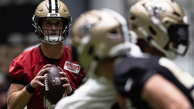 Tyler Shough gets ready to throw the ball as teammates in gold helmets stand in the foreground at Saints OTAs.