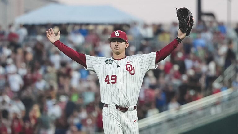 A baseball player in a white pinstripe Bulldogs uniform, number 49, raises both arms on the field as the crowd watches in the background.