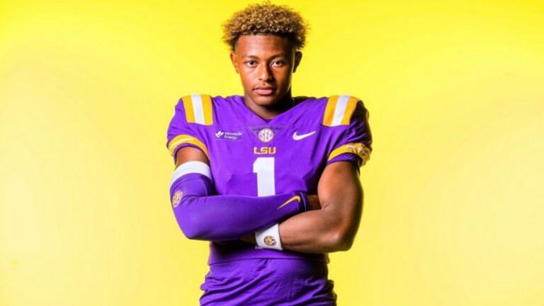 An LSU football player wearing number 1 stands with arms crossed against a bright yellow background, looking confident and ready.