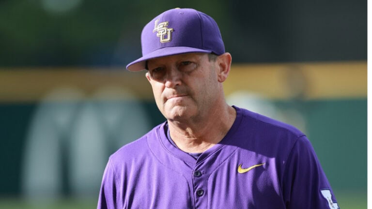 A man wearing a purple LSU baseball uniform and cap stands outside, gazing ahead with a calm, neutral expression.