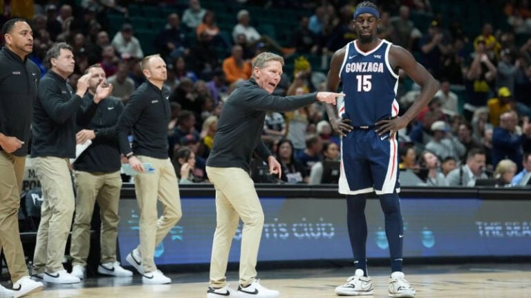 A Gonzaga basketball coach gestures while talking to a player on the court as spectators look on during the game.
