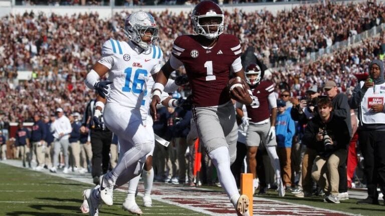 A Mississippi State player in maroon runs the ball down the sideline with a defender in white close behind.