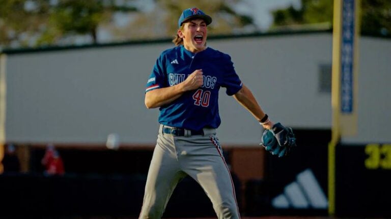 A baseball player in a blue LSU jersey, number 40, celebrates with a fist pump and shout after pitching during a game.
