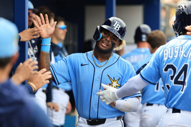 A Tampa Bay Rays player high-fives teammates in the dugout, celebrating energetically after a big play.
