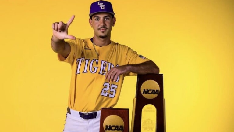 An LSU baseball player stands next to two NCAA trophies, making an "L" shape gesture—ideal for a profile like Jason Wachs.