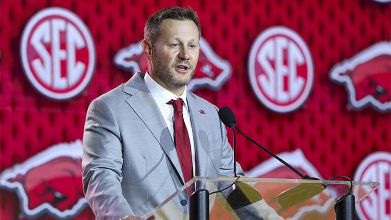 Ryan Silverfield speaks at a podium, with SEC stocks and Razorbacks logos visible in the background.