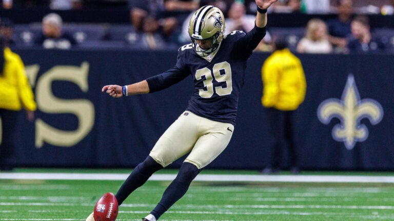 A Saints player in black and gold kicks off as fans and security watch from the sidelines, determining his team's starting field position.
