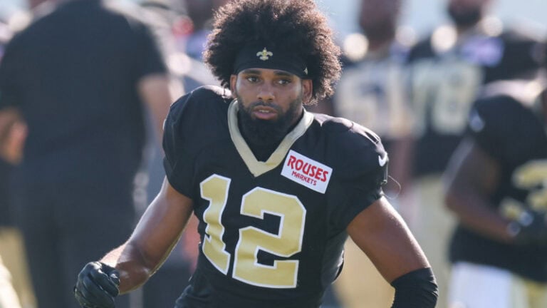 Chris Olave, number 12 for the Saints, wears gloves and practices on the field in his black and gold uniform.