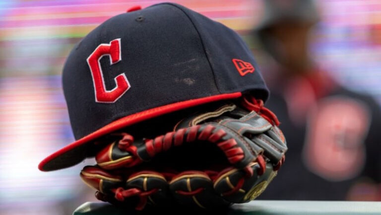 A navy baseball cap with a red "C" sits atop a black and brown glove.
