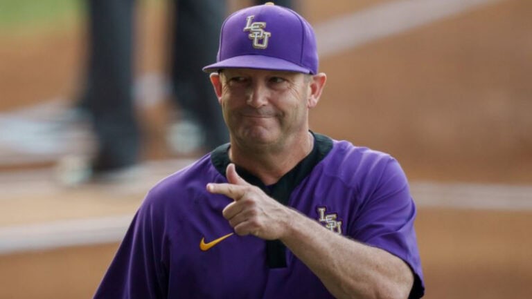A smiling man in an LSU Tigers baseball uniform points while standing on the field, clearly a standout player for the team.