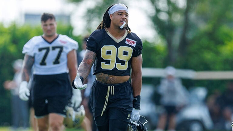 Chase Young walks outside at Saints camp in practice jerseys, helmets in hand.