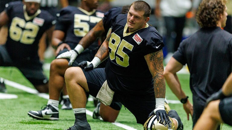 John Ridgeway III stretches at training camp, with one kneeling in the foreground as position battles intensify.