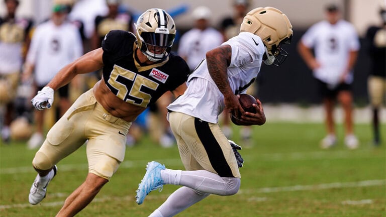 Saints defenders in black pursue a white-jersey runner with the ball during practice on the field.