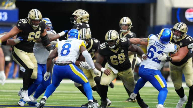 Saints football players face off at the line of scrimmage during an NFL game on a turf field.