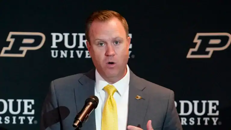 A man in a suit and yellow tie speaks at a podium labeled “MARLER RANT,” with a Purdue University backdrop behind him.