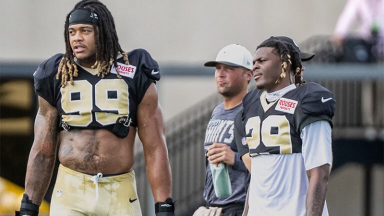 Two football players in black and gold pose with a casually dressed fan during Day 9 of Saints Training Camp.