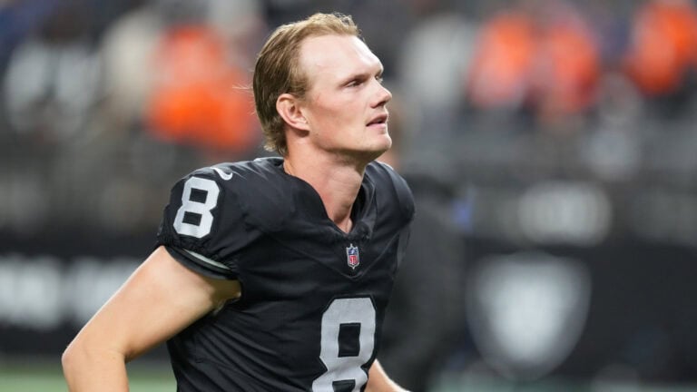 A football player in a black number 8 jersey stands on the field, glancing sideways with stadium lights and fans behind him.