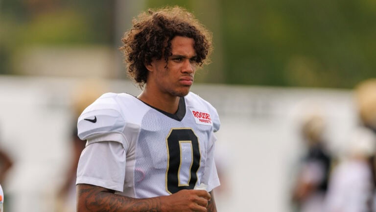 A football player in a white jersey numbered 0 stands outside during practice, gazing ahead with a serious look.