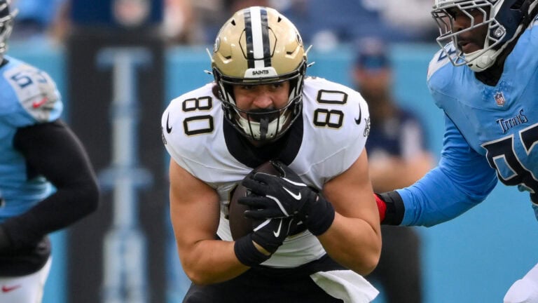 A Saints football player runs with the ball as a Titans defender chases, capturing an action-packed moment reminiscent of Ty Chandler.