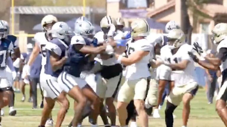 Players from the Cowboys and Saints get into a heated brawl during joint practice on a grassy field.