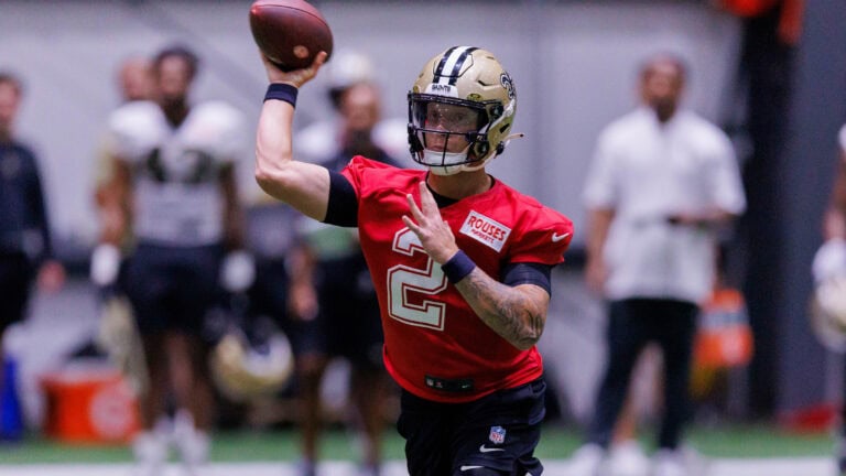 Spencer Rattler throws a pass at Saints practice while teammates and coaches look on in the background.