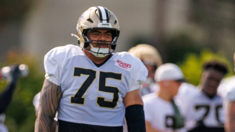 A football player wearing a white number 75 jersey stands outdoors at Saints camp, day 11—considered a key player this season.