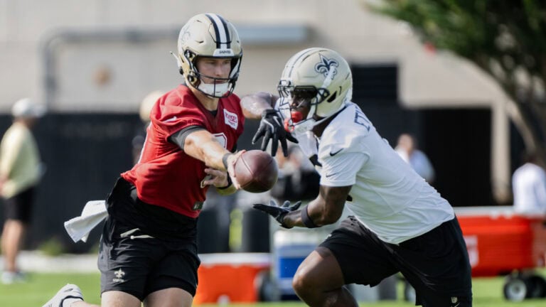 Two football players in pads run a handoff drill at Saints Training Camp on the field.