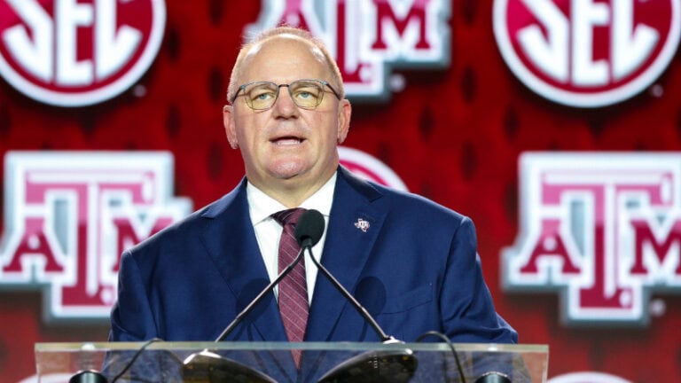 A man in a suit stands at a podium, asking questions, with Texas A&M and SEC logos visible behind him.