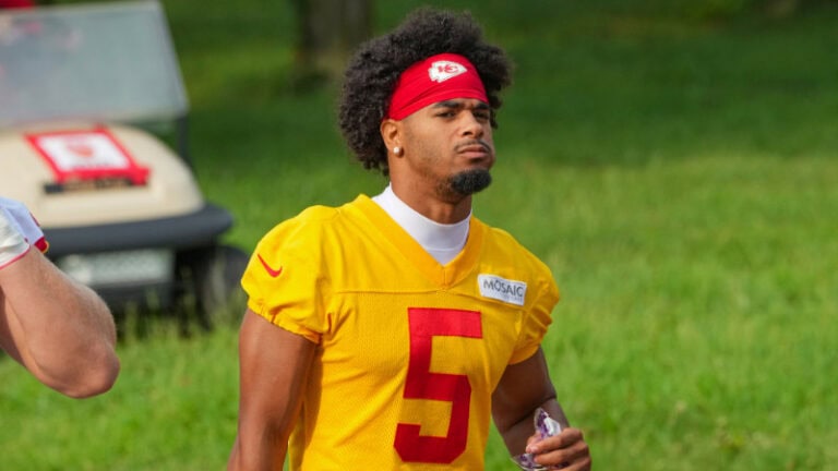 LSU cornerback Mansoor Delane stands in a yellow number 5 jersey and red headband, with grass and a golf cart in the background.