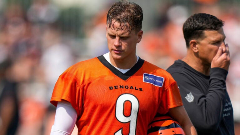Joe Burrow, wearing Bengals jersey number 9, holds his helmet next to another player during outdoor practice.