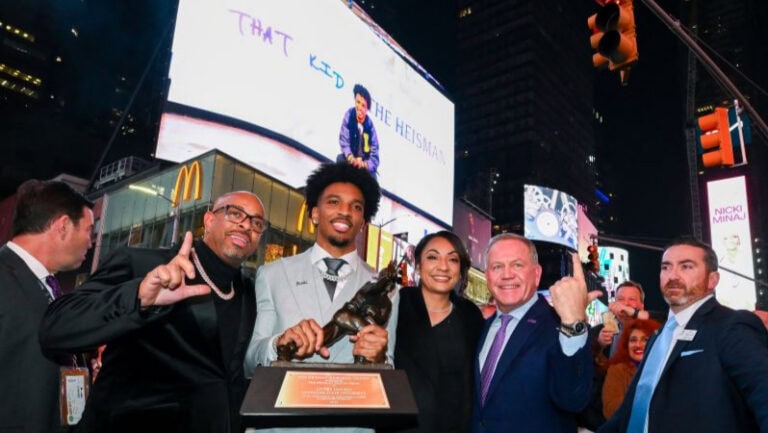 Daniels and PALMER smile with a trophy in Times Square at night, colorful billboards and lively crowds glowing in the background.