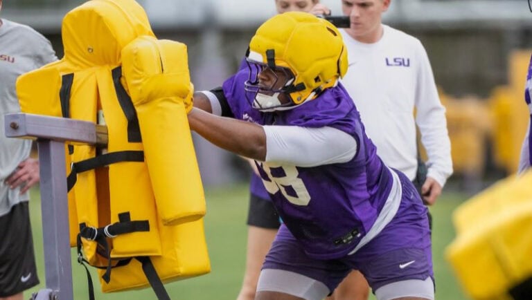 A freshman football player in purple and yellow practices blocking on a padded dummy during fall camp.