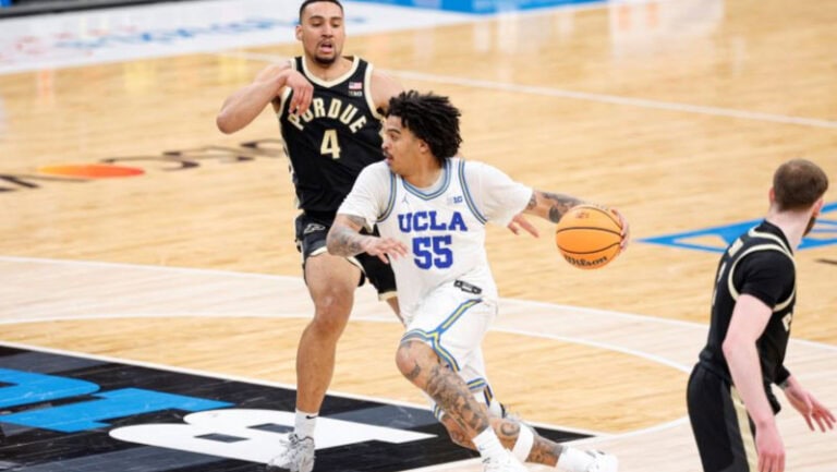 Skyy Clark of UCLA dribbles past a Purdue defender on the basketball court during a game.