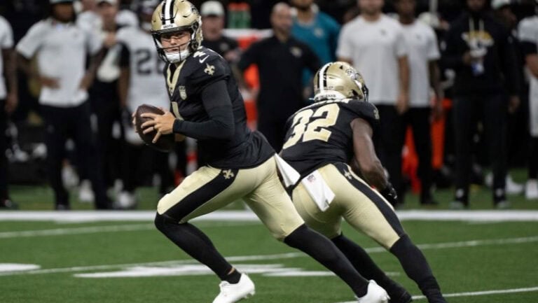 Saints quarterback Wilson readies to throw during the preseason opener, both players wearing classic black and gold uniforms.