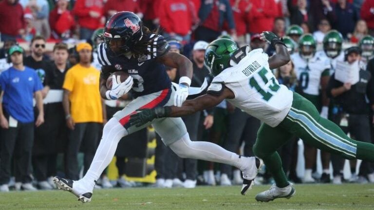 An LSU player in a dark uniform runs with the football as a defender in white attempts to tackle him, highlighting veteran impact.