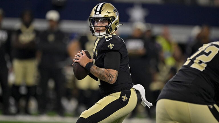A Saints player in a new black and gold uniform stands ready to throw as teammates look on nearby.
