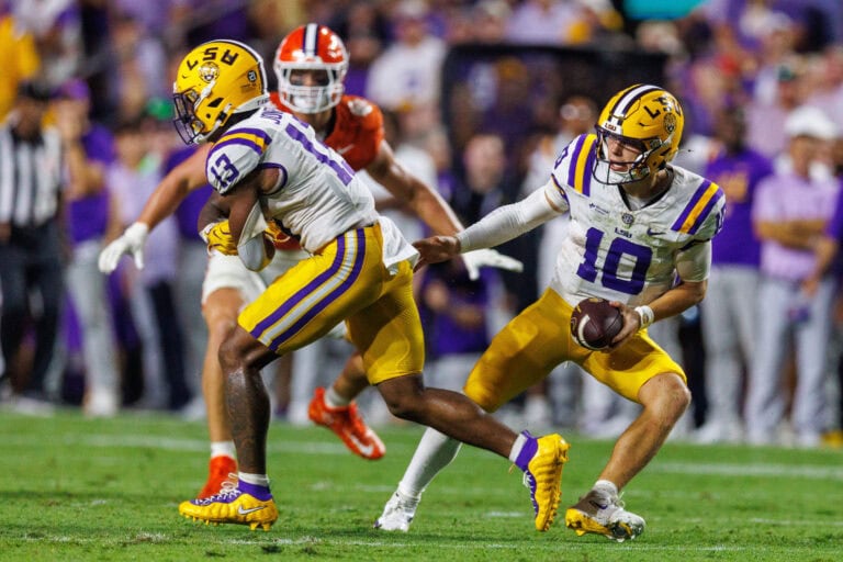 An LSU football player hands off the ball during a game against a team in orange uniforms.