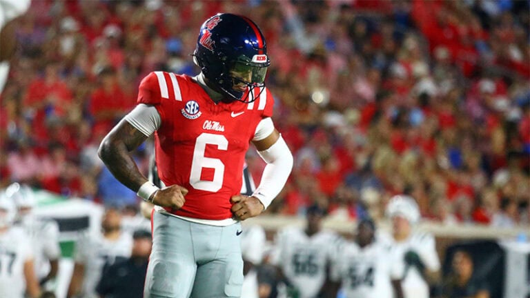 Trinidad Chambliss stands on the field in a red Ole Miss jersey, number 6, flexing his arms confidently.