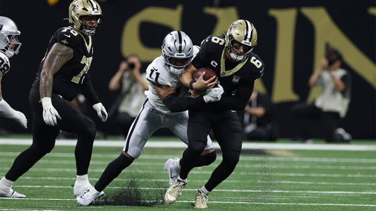 A Raiders player in white brings down a Saints ball carrier in black during an intense game on the field.