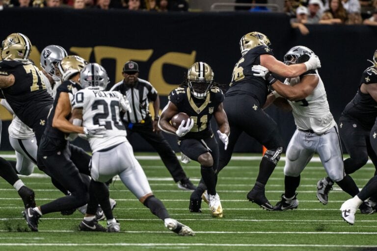 A Saints player in black runs with the ball as teammates block Raiders defenders, hinting at a tense fourth quarter.