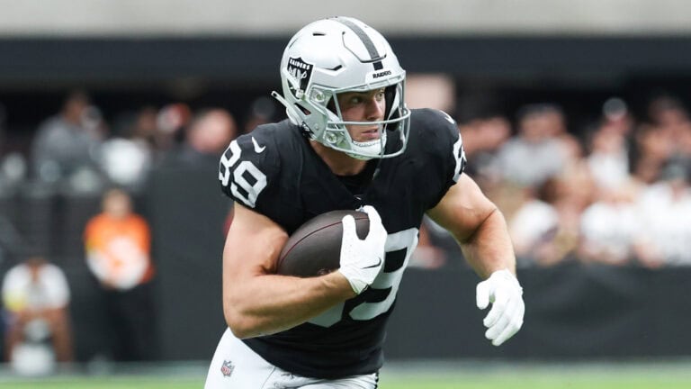 A football player in black and silver sprints down the field with the ball, helmet and gloves on during a game.