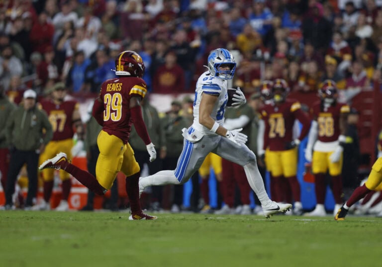 A player in a white uniform sprints with the ball as an Arizona Cardinals player in red and yellow races after him during a game.