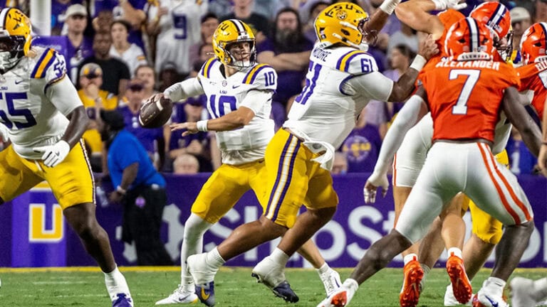 An LSU quarterback readies to throw the football as he faces off against opponents in orange uniforms during a game.