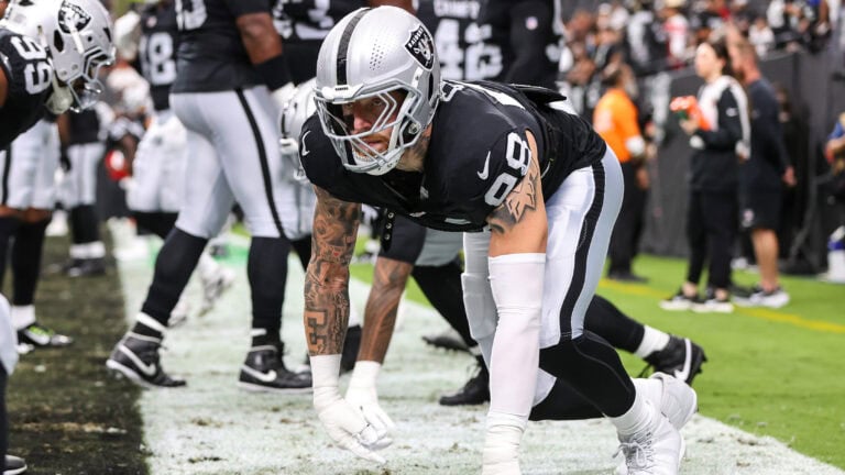 A Raiders football player crouches on the sideline, getting ready for the game as teammates and coaches watch nearby.