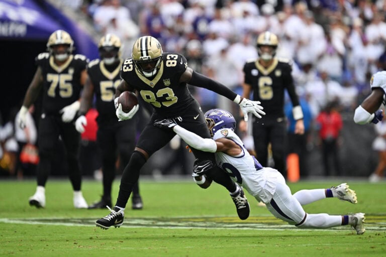 Juwan Johnson of the Saints, in a black uniform, races downfield with the ball, dodging a diving defender for extra yards.